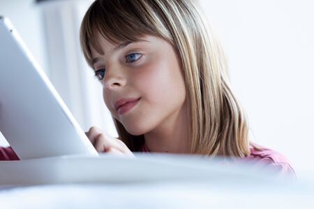 Close-up of pretty concentrated little girl using her digital tablet at home.の写真素材