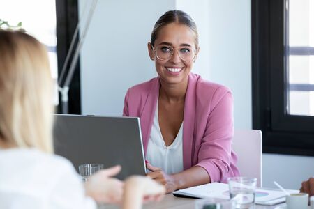Shot of smiling young business woman listening her partner while working with laptop on coworking space.の写真素材