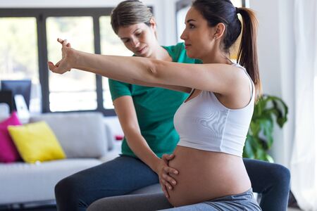 Shot of physiotherapist helping to beautiful pregnant woman for doing pilates exercises with ball...