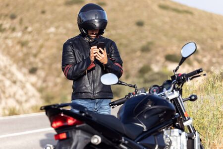 Shot of man biker talking on the phone to the insurance of his motorcycle after having suffered a breakdown on the road.の写真素材