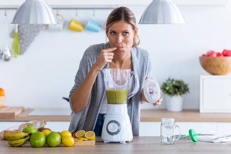 Shot of pretty young woman tasting the detox juice she just made with the blender at home.の写真素材