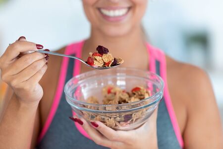 Close-up of smiling young woman eating cereals with strawberries at home.