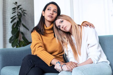 Shot of pretty young woman supporting and comforting her sad friend while sitting on the sofa at home.の写真素材