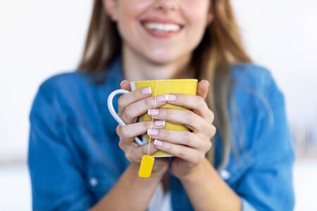Close-up of pretty young woman holding a cup of tea in the kitchen at home.
