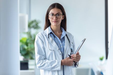 Portrait of pretty young female doctor looking at camera while standing in the office.の写真素材