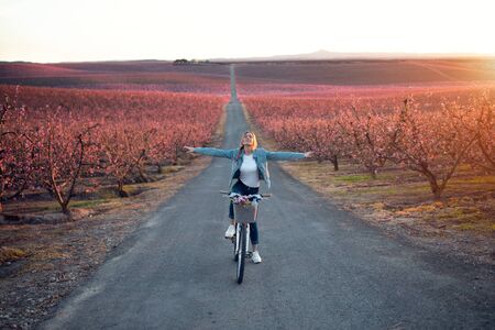 Shot of pretty young woman with a vintage bike enjoying the time in cherry field in springtime.