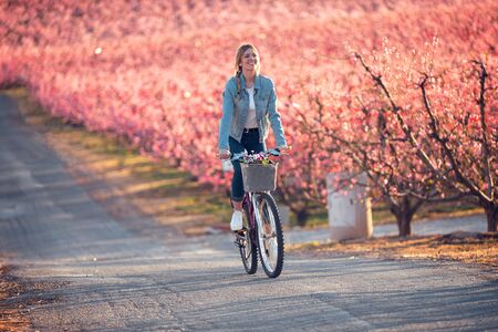 Shot of pretty young woman riding with a bike in cherry field in springtime.の写真素材