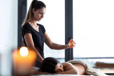 Shot of beautiful young woman applying hot wax from a candle for back massage to a pretty woman on the spa center.の写真素材