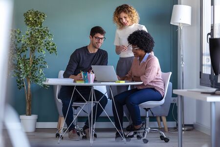 Shot of casual young business people working with laptop and talking of they new project together in...