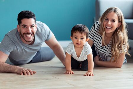 Portrait of pretty young parents looking at camera while playing with baby son at home.