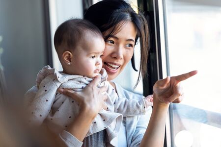 Shot of happy young mother with little baby girl looking through the window at home.の写真素材