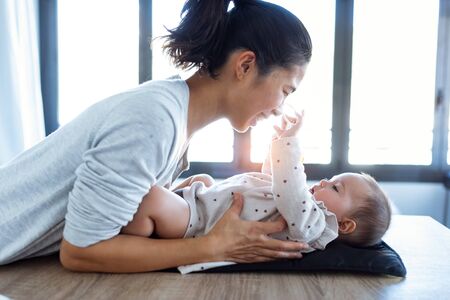 Shot of smiling young mother has fun with little baby while changing his nappy at home.