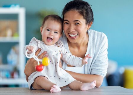 Shot of happy young mother with her baby daughter looking at camera while staying at home.