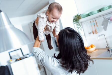 Shot of happy young mother lifting her cute daughter up high in air while spending and enjoying time together at home.の写真素材
