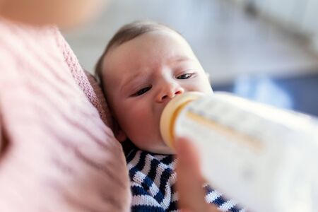 Close-up of mother feeding her baby son with feeding bottle while sitting on sofa at home.の写真素材