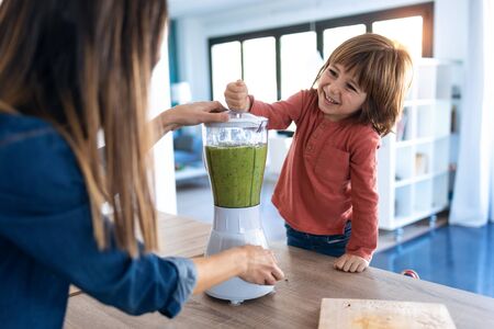 Shot of boy helping his mother to prepare a detox juice with blender in the kitchen at home.の写真素材