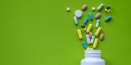 Shot of white bottle and multi-colored pills on a green background. Concept of pharmaceuticals, medicine, drugs and treatment for diseases.の写真素材