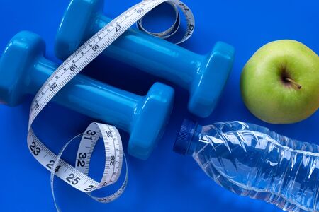 Top view of blue dumbbells, water bottle, green apple and measuring tape on blue background. Healthy lifestyle concept.の写真素材
