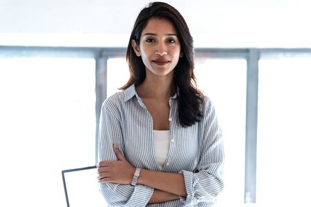 Shot of elegant young business woman looking at camera while standing in the office.の写真素材