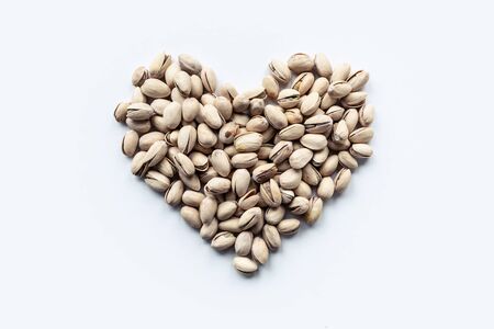 Shot of pistachio nuts forming a heart-shape on white background.