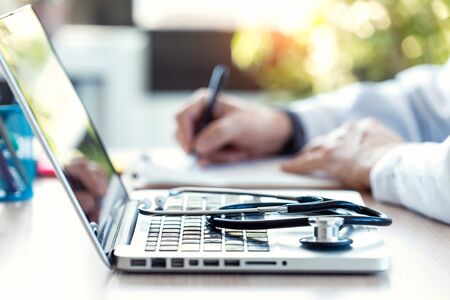 Close-up of a medical stethoscope on laptop keyboard. Blur background of a doctor reviewing...