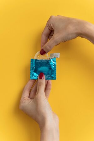 Close-up of young woman holding condom ready to use for safe sex over yellow background.