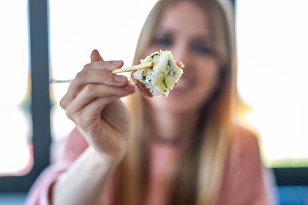 Shot of pretty young woman showing sushi to camera while sitting in front of a window in the office.の写真素材