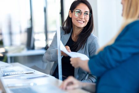 Shot of two business women passing documents with keeping a distance in the office.の写真素材