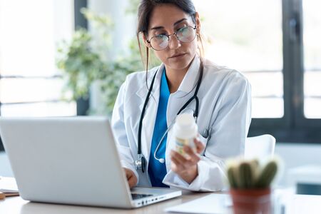 Shot of concentrated female doctor writes the medical prescription in a laptop in the consultation.の写真素材