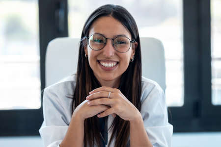 Portrait of happy young female doctor smiling and looking at camera while sitting in the...