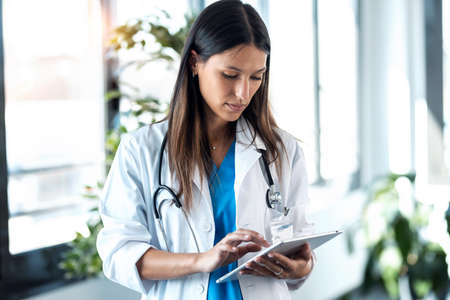 Shot of confident young female doctor reviewing the patient's medical history on her digital tablet while standing in the consultation.の写真素材