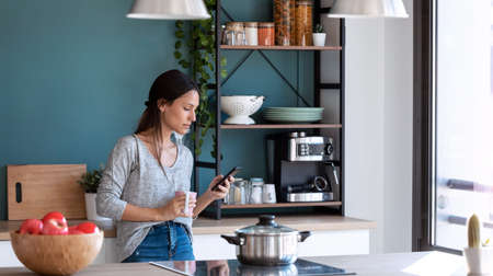 Shot of tired young woman suffering neck pain while sitting on the stool in the kitchen at home.の写真素材