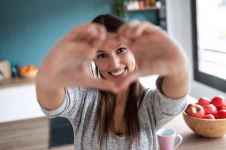 Shot of smiling young woman using her mobile phone while eating yogurt in the kitchen at home.の写真素材