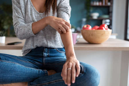 Shot of smiling young woman using her mobile phone while eating yogurt in the kitchen at home.
