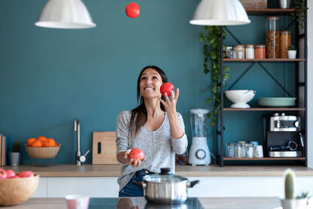 Shot of smiling young woman using her mobile phone while eating yogurt in the kitchen at home.