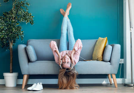 Shot of motivated young woman listening to music with smartphone while lying down on sofa at home.の写真素材