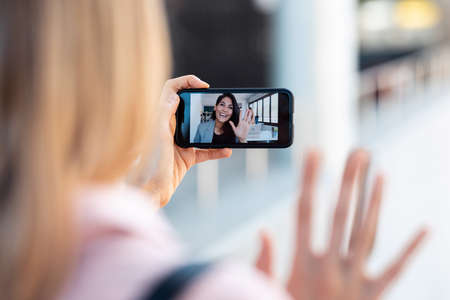 Shot of back view of woman having video conversation with pretty young business woman while staying in the street.の写真素材