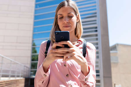 Shot of smiling young woman using her mobile phone while standing in the street.の写真素材