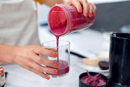 Close up of young nutritionist woman serving healthy handmade smoothie in a cup in kitchen at home.