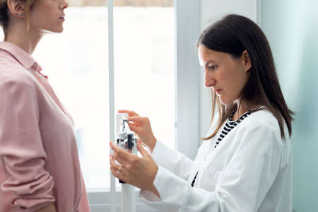Shot of beautiful young nutritionist woman weighing and measuring his patient on the scale in consultation.の写真素材