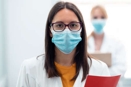 Portrait of professional young female doctor in medical mask looking at camera in the hospital.の写真素材