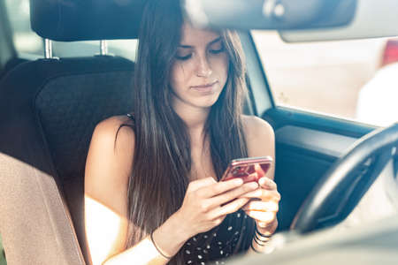 Portrait of beautiful young woman sending messages with her mobile phone in the car.の写真素材