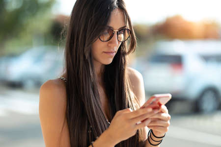 Shot of cheerful young woman using her mobile phone while standing in the street.の写真素材