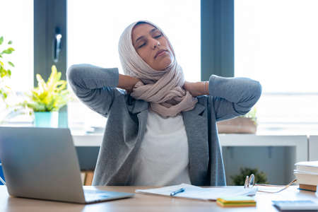 Shot of tired young muslim business woman wearing hijab with neck pain at the office.