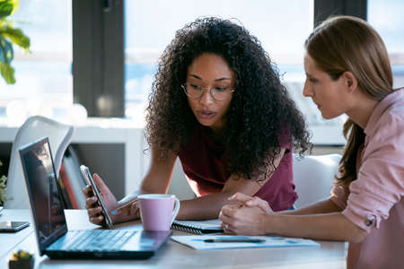 Shot of two beautiful business women working together with laptop while talking about job news in the office.の写真素材