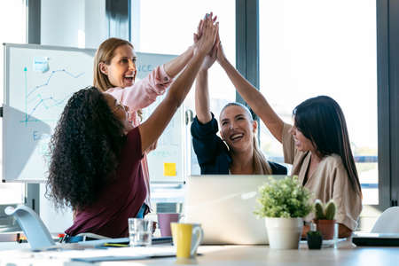 Shot of group of successful smart business women holding up their right hands on coworking place.