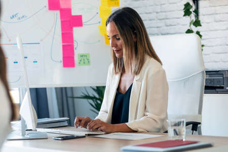 Shot of confident business woman working with computer while reading some notes in the office.の写真素材