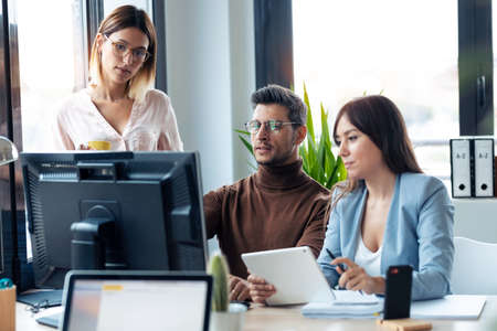 Shot of successful young business team standing around computer doing a video call in the coworking...
