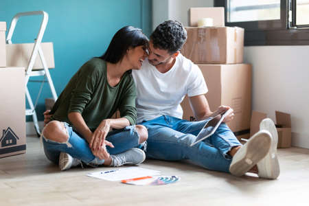 Shot of cute couple kissing each other while looking ideas to decorate the new apartment in digital...