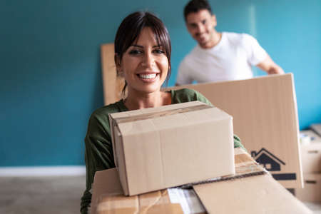 Shot of beautiful young couple holding cardboard boxes while moving to new home. Looking at camera.